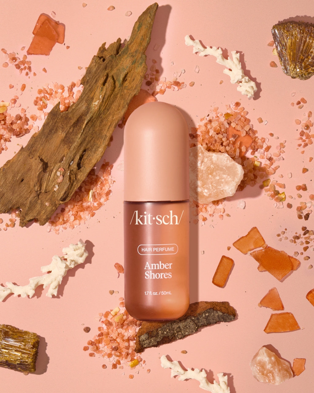 Flat lay of Kitsch Hair Perfume in scent "Amber Shores" Surrounded by items like pink Himalayan salt, driftwood, amber, and dried coral