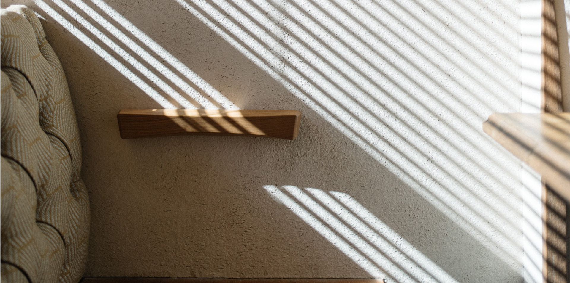 The Annex sun rays through blinds onto a white wall with wood shelf accents and a couch cushion back